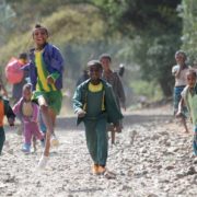 Kinder in Mekerie rennen und hüpfen auf der Straße lachend auf die Kamera zu