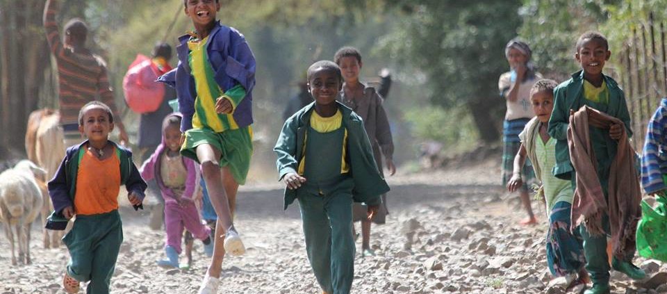Kinder in Mekerie rennen und hüpfen auf der Straße lachend auf die Kamera zu